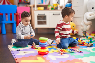 Two kids playing xylophone holding car toy sitting on floor at kindergarten