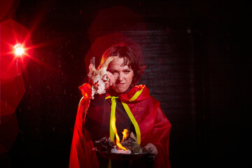 Witch woman in red cloak with skull on black background and light in night. Female warrior in the Dark