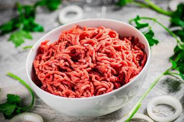 Minced meat in a bowl on a table with parsley and onion rings. 