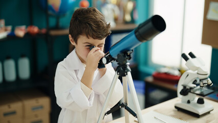Adorable hispanic boy student using telescope at laboratory classroom