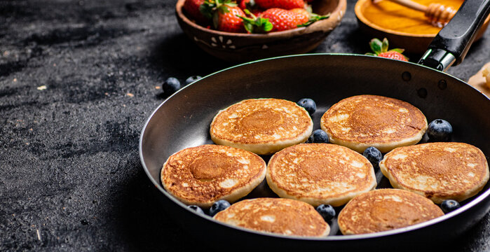 Pancakes in a frying pan with fresh berries and honey. 