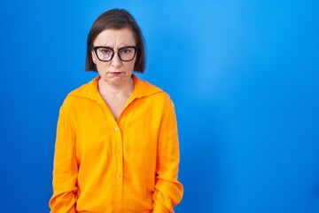 Middle age hispanic woman wearing glasses standing over blue background skeptic and nervous, frowning upset because of problem. negative person.