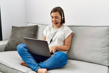 Middle age hispanic woman sitting on the sofa wearing headset at home