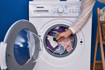 Middle age woman pouring detergent on washing machine at laundry room
