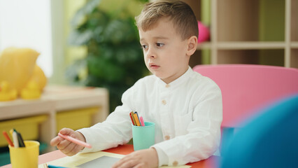 Adorable caucasian boy student sitting on table drawing on paper at kindergarten