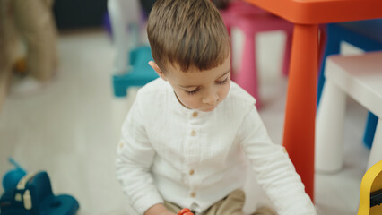 Adorable caucasian boy student sitting on floor with relaxed expression at kindergarten