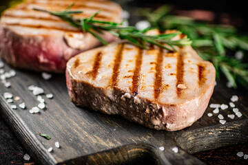 Grilled tuna on a cutting board with a sprig of rosemary. 