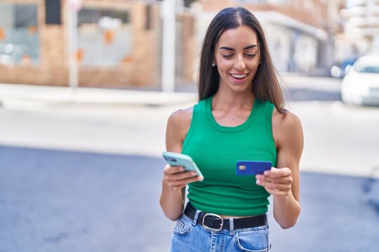 Young beautiful hispanic woman using smartphone and credit card at street