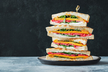 Big homemade sandwich with sausage, cheese and arugula on a dark concrete background