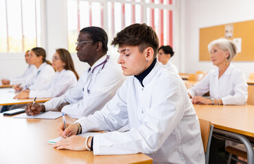 Doctors of different ages sit at their desks and listen carefully to teacher in advanced training class of the medical university