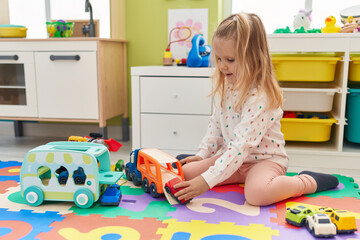 Adorable blonde girl smiling confident playing with car toys at kindergarten