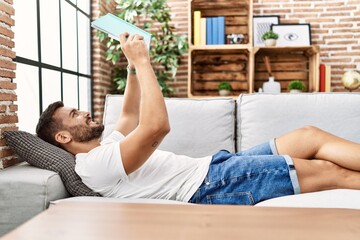 Young hispanic man smiling confident reading book at home