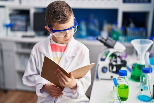 Blond child wearing scientist uniform reading book at laboratory