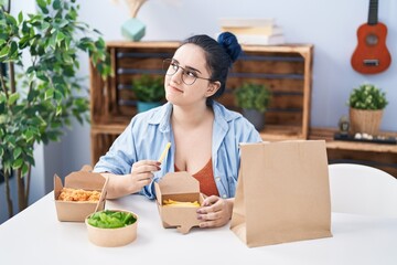 Young caucasian woman eating take away food sitting on table at home