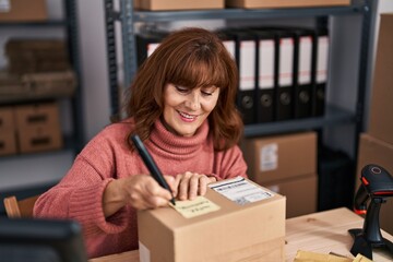 Middle age woman ecommerce business worker writing on package at office