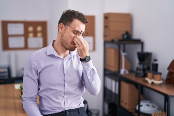 Young hispanic man at the office tired rubbing nose and eyes feeling fatigue and headache. stress and frustration concept.