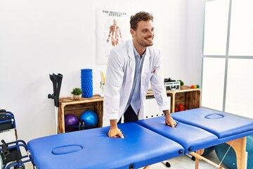 Young hispanic man wearing physiotherapist uniform standing at clinic