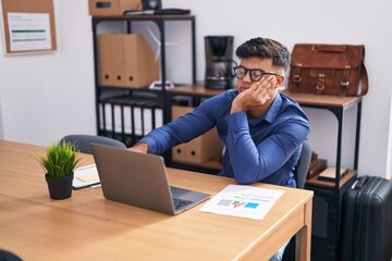 Young hispanic man business worker using laptop with serious expression at office