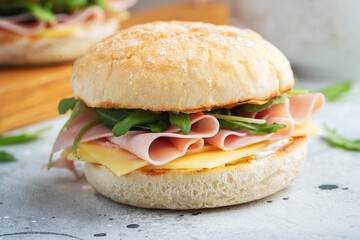 Two homemade sandwiches with ham, cheese and arugula on a concrete table.