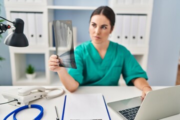 Young beautiful hispanic woman doctor using laptop looking xray at clinic