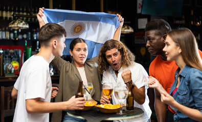 Group of Argentina football team fans spending time in bar, drinking bear and having fun. People...