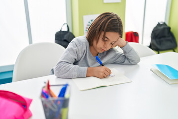 Adorable hispanic boy student writing on notebook at classroom