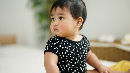 Adorable hispanic baby sitting on bed at home