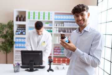 Two hispanic men pharmacist and client using computer reading medication label bottle at pharmacy
