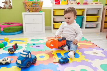 Adorable caucasian baby playing with truck toy sitting on floor at kindergarten