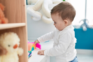Adorable caucasian baby playing with construction blocks standing at kindergarten
