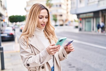 Young blonde woman using smartphone and credit card at street