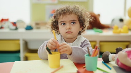 Adorable hispanic girl preschool student sitting on table drawing on paper at kindergarten