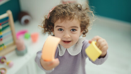Adorable hispanic girl playing with construction blocks standing at kindergarten