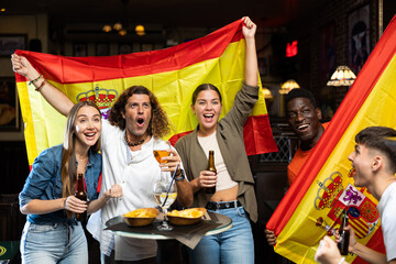 Naklejka premium Group of excited Spanish football fans having fun in sports bar, celebrating victory of favorite team together after watching match