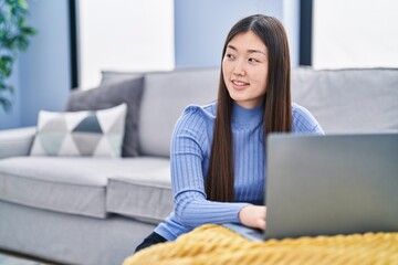 Naklejka premium Chinese woman using laptop sitting on floor at home
