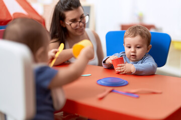Obraz na płótnie Canvas Teacher and preschool student sitting on table learning to eat at kindergarten