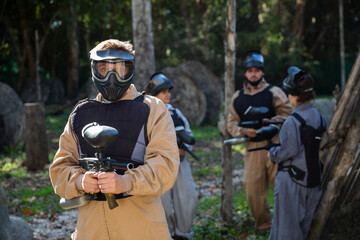 Fototapeta premium Man and his paintball sport team in protective uniform at paintball shooting range
