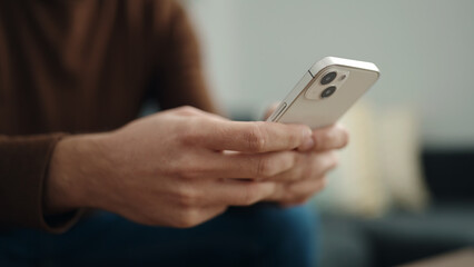 Young hispanic man using smartphone sitting on sofa at home