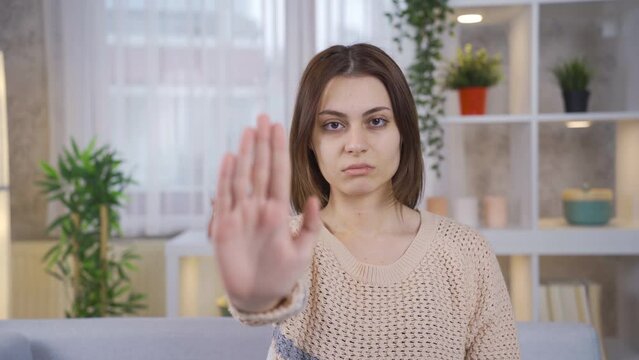 At home, young woman says stop with her hand against abuse and rape and looks at the camera without fear.
Young woman making a stop sign with her hand against abuse and rape.
