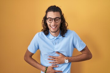 Young hispanic man standing over yellow background smiling and laughing hard out loud because funny...