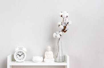 Buddha figurine, alarm clock, lotus candlestick and vase with branch of cotton on white shelf. Concept mental health and recreation. Selective focus, space for text