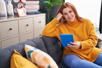 Young beautiful plus size woman using touchpad sitting on sofa at home