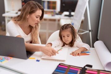 Teacher and toddler sitting on table drawing on notebook at classroom