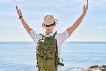 Young caucasian man tourist standing with arms open on back view at seaside