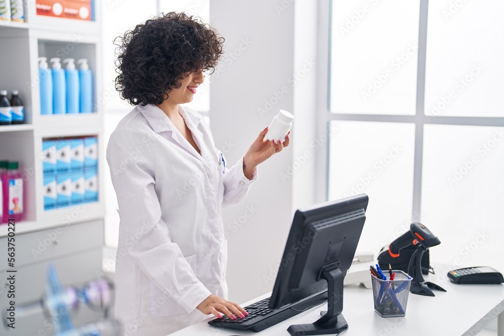 Poster Young middle east woman pharmacist using computer holding pills at pharmacy