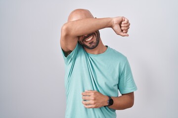 Middle age bald man standing over white background covering eyes with arm smiling cheerful and funny. blind concept.