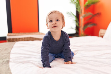 Adorable blond toddler sitting on bed with with relaxed expression at bedroom