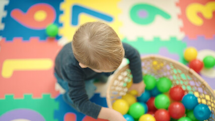 Adorable blond toddler playing with balls sitting on floor at kindergarten