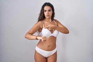Fototapeta premium Young hispanic woman wearing white lingerie in hurry pointing to watch time, impatience, upset and angry for deadline delay