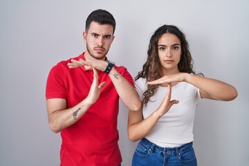 Young hispanic couple standing over isolated background doing time out gesture with hands, frustrated and serious face